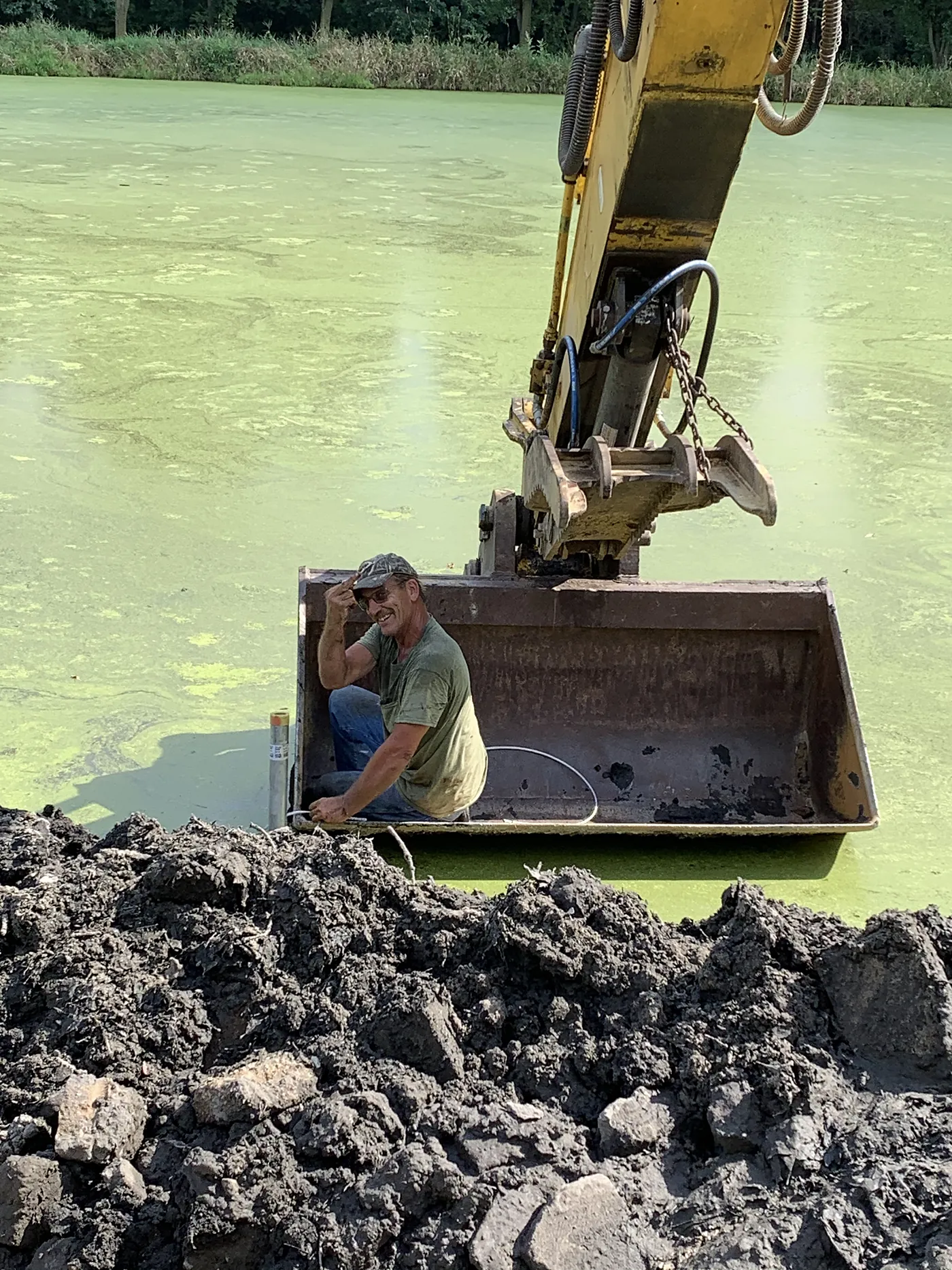 Salz operator in an excavator bucket beside a pond under construction
