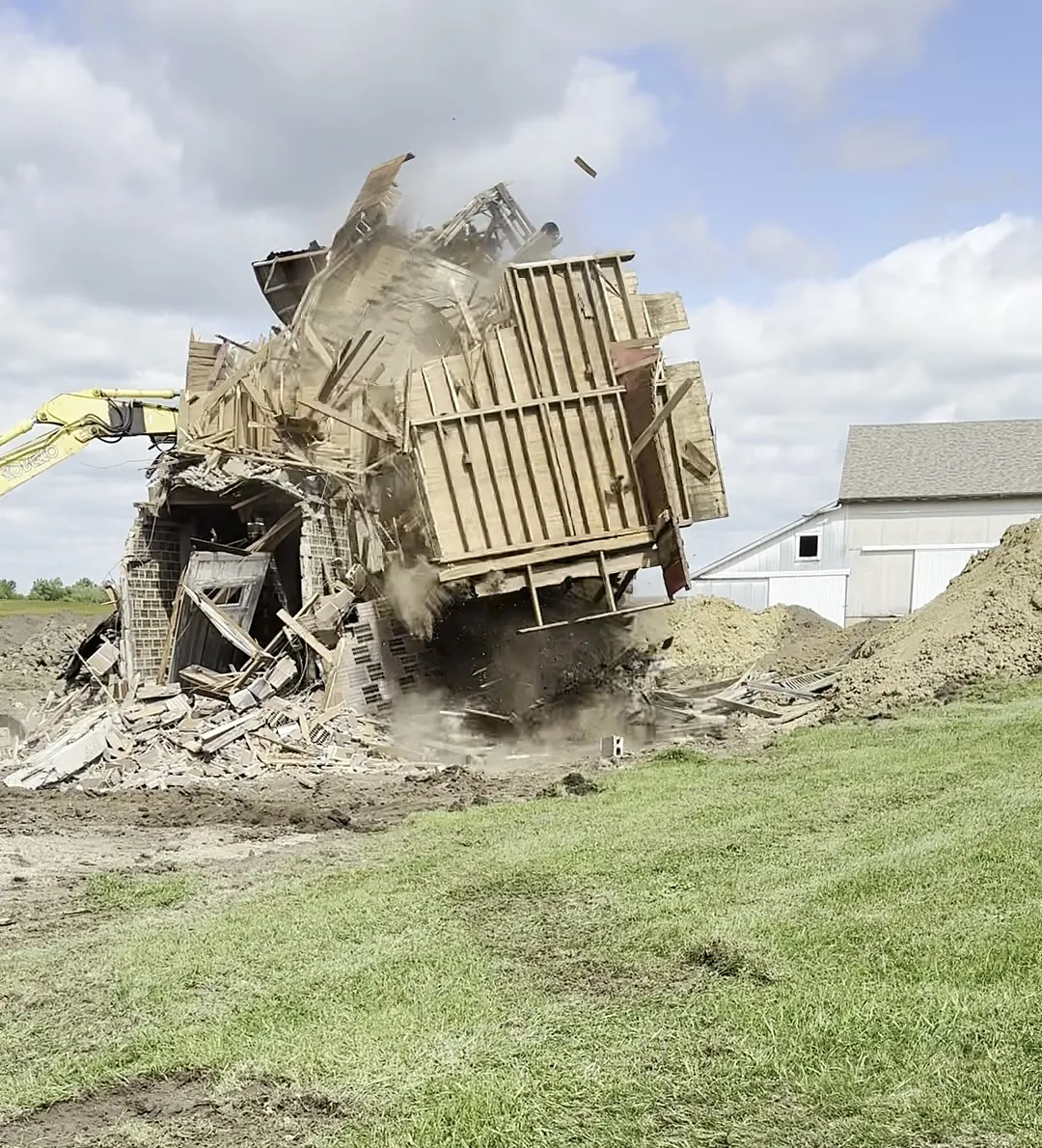 The upper frame collapsing toward the excavator in a cloud of dust